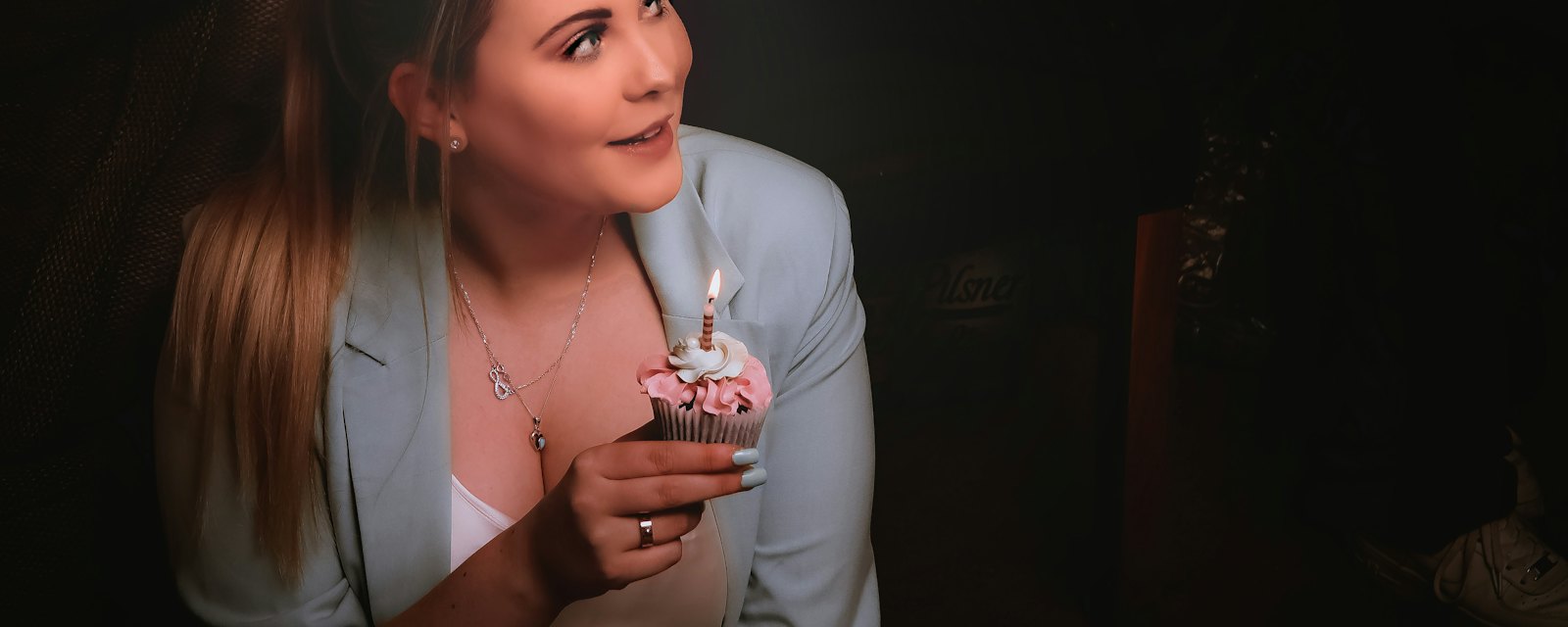 A young woman smiling at a cupcake with a lit birthday candle