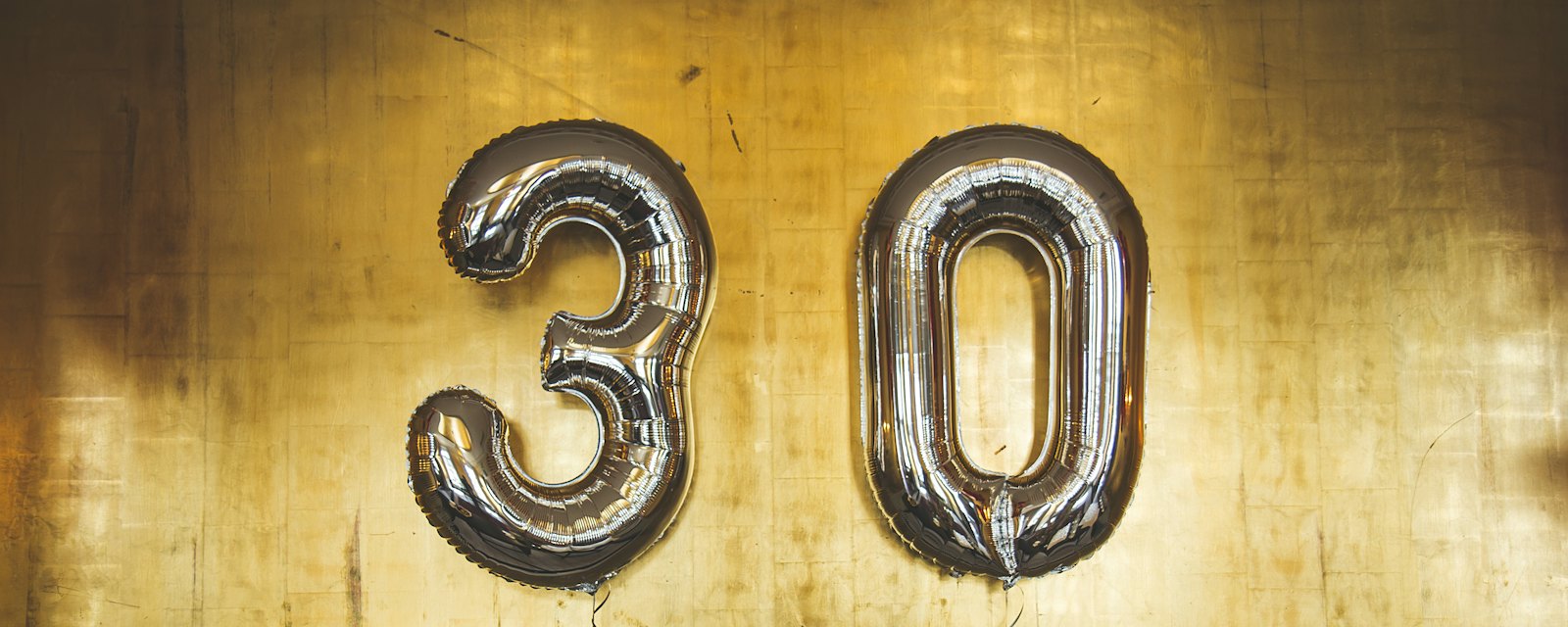 Silver number 30 balloons against a gold wall