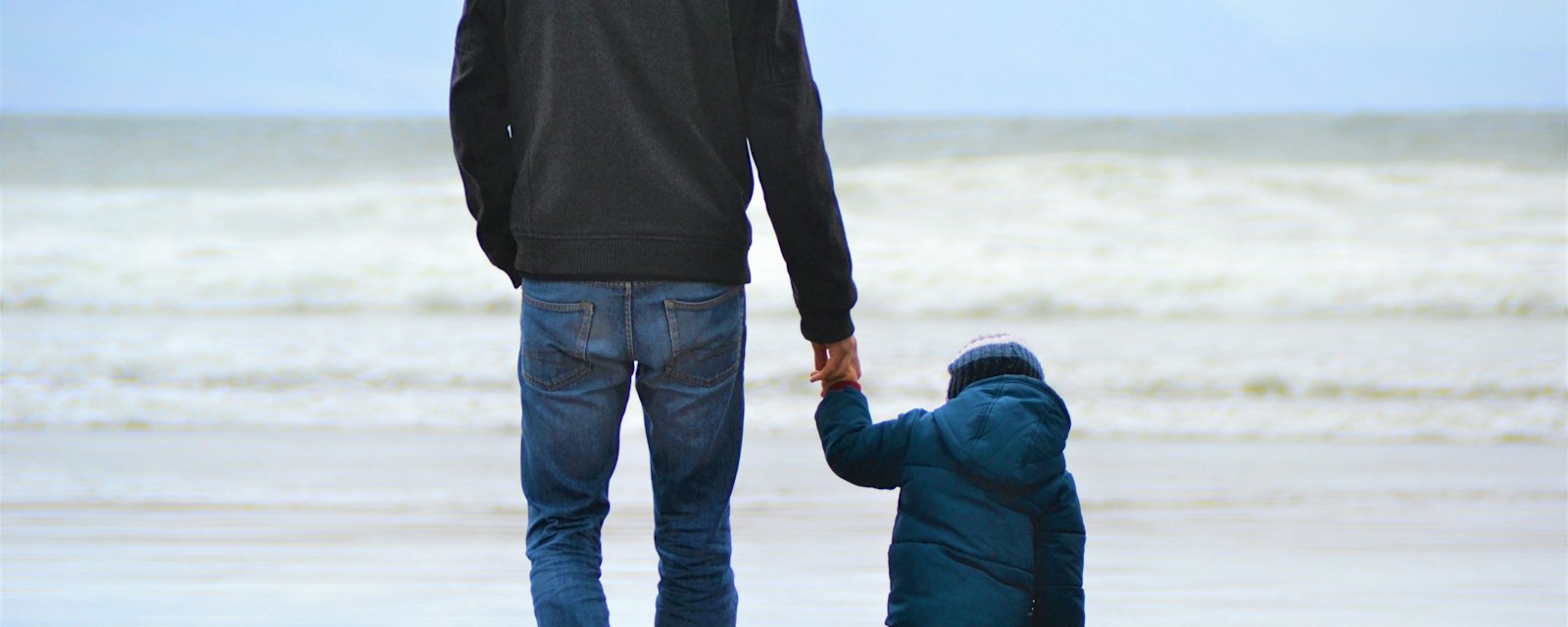 A father holding his young son’s hand on a beach