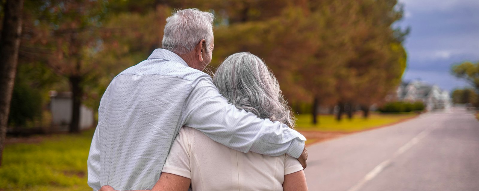 An older couple walking arm in arm down a country road