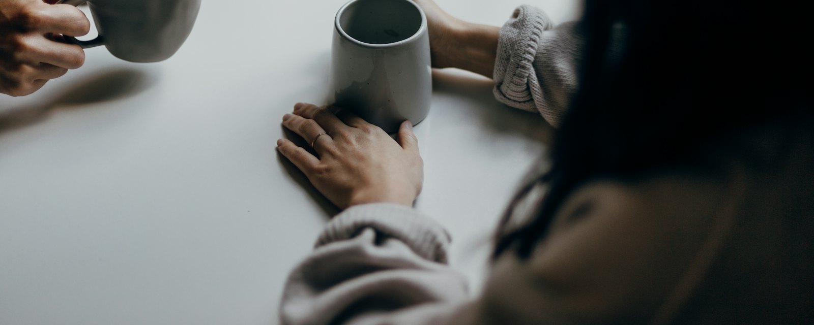 Two people sitting together at a table holding mugs of tea