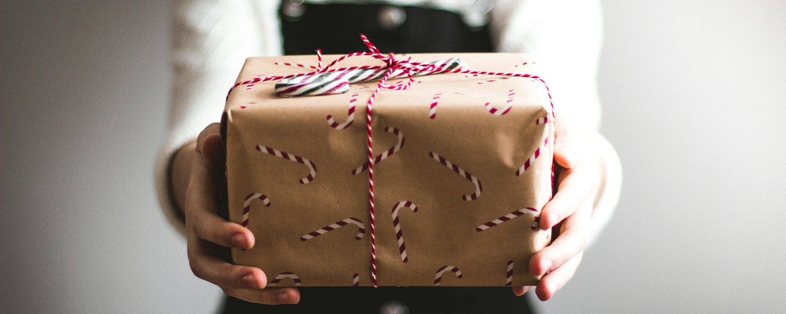 Hands holding out a brown-paper wrapped present tied with string