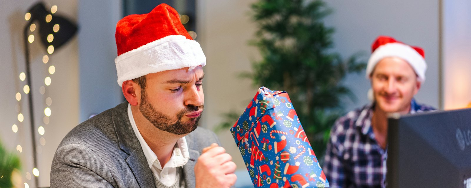 Colleagues in Santa hats opening a wrapped present at an office party