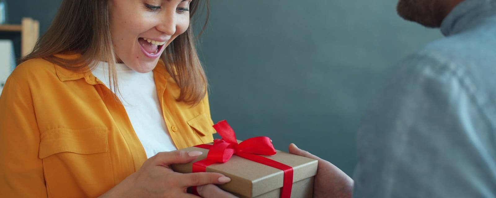 A delighted woman opening a gift wrapped in red ribbon