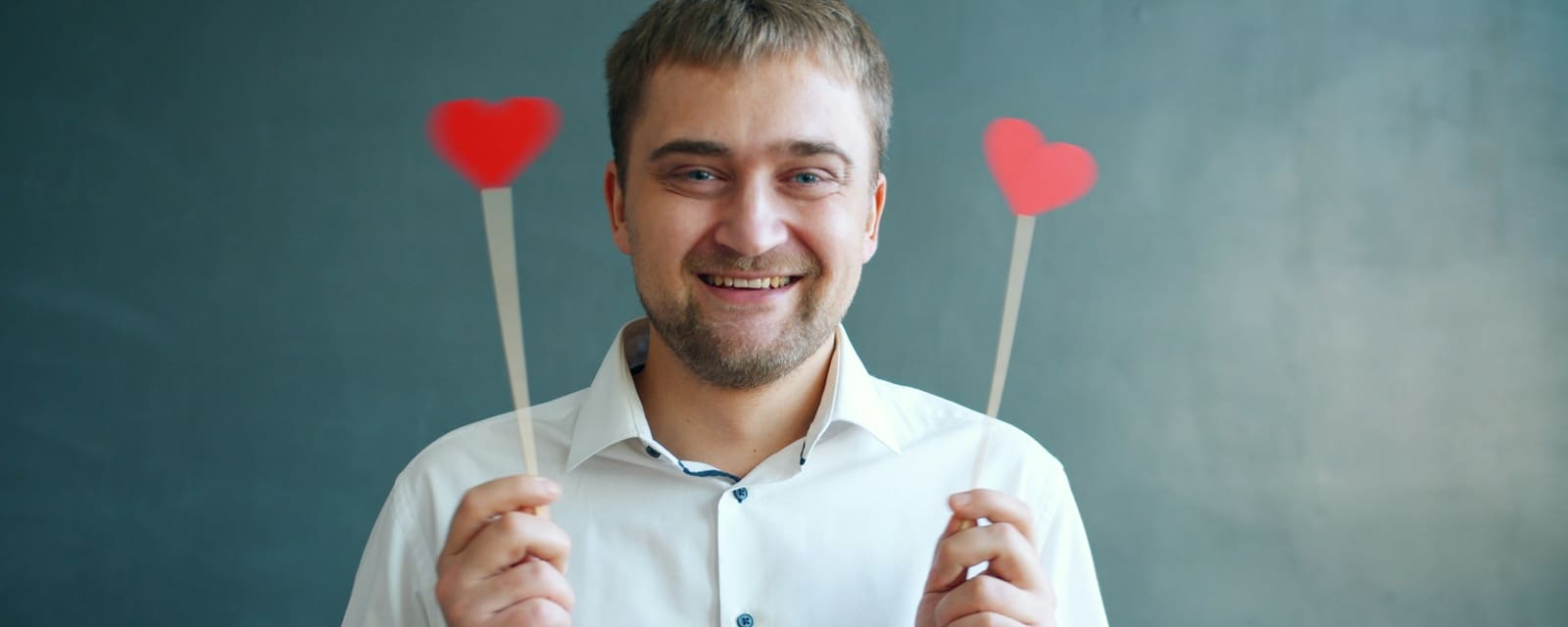 A smiling man holding up two red paper hearts