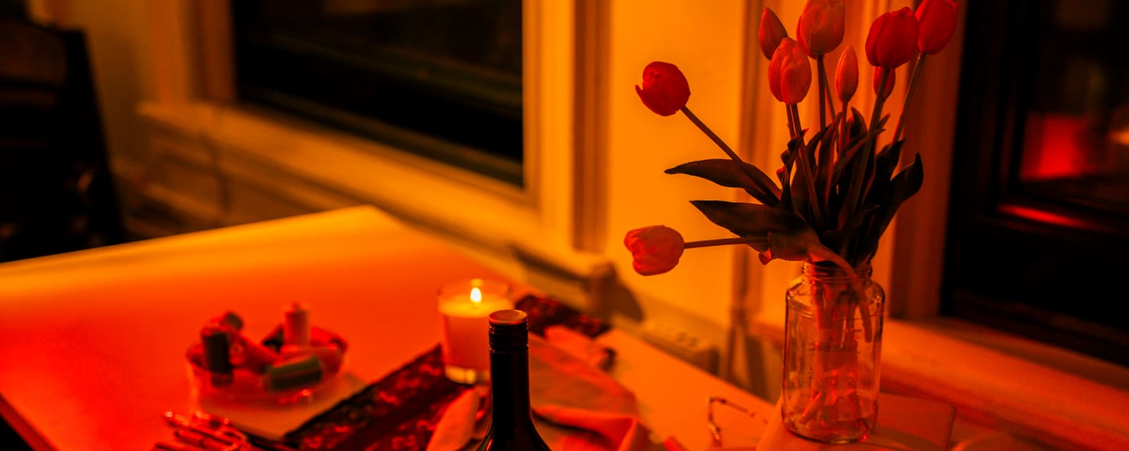 A candlelit table at home with tulips, red wine and a lit candle