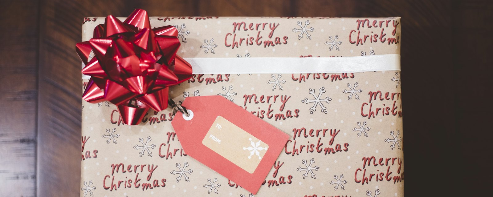 A Christmas present wrapped in Merry Christmas paper with a red bow and gift tag