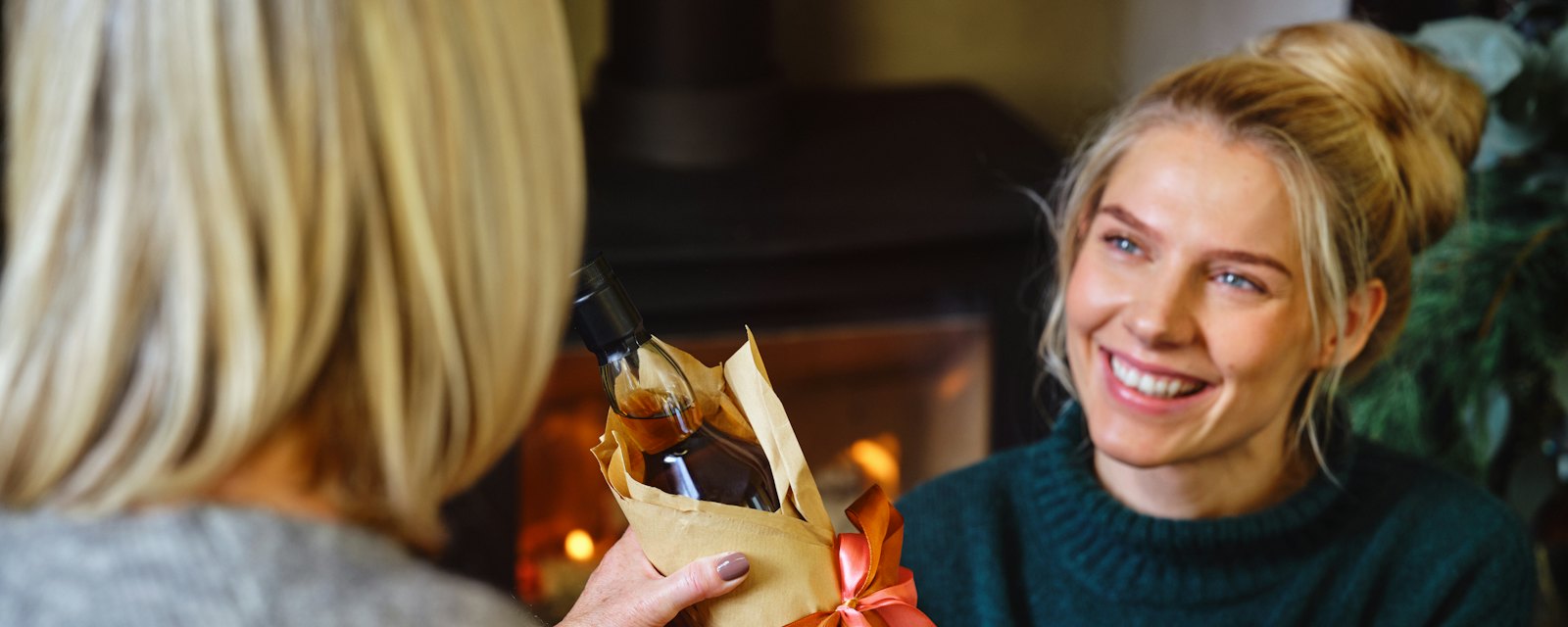 A smiling woman being handed a wrapped Christmas present by the fire