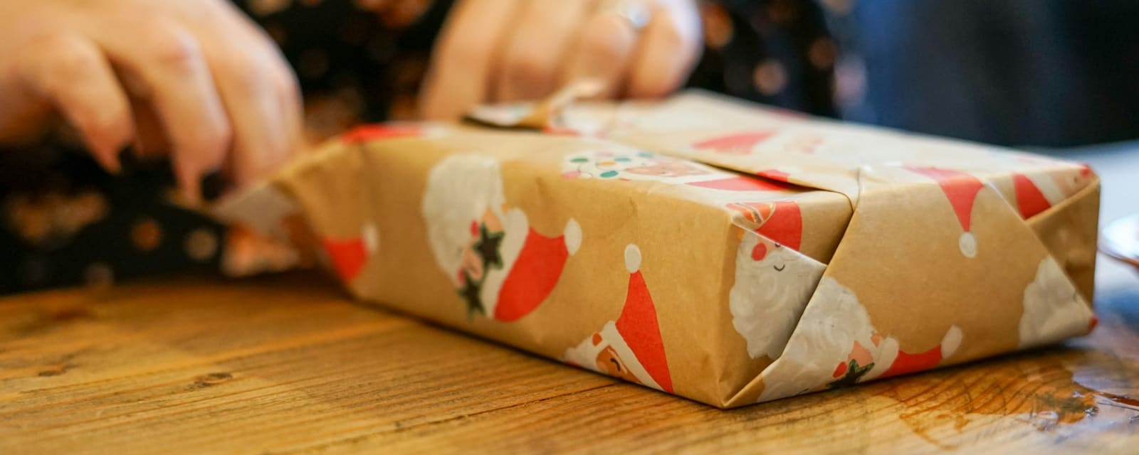 Hands wrapping a Christmas present in printed brown paper on a wooden table