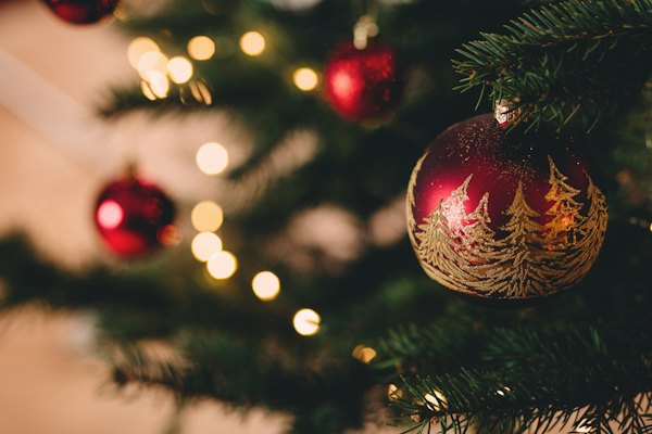 A red bauble hanging on a lit Christmas tree