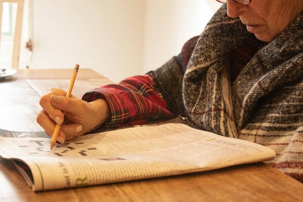 Someone filling in a newspaper crossword with a pencil