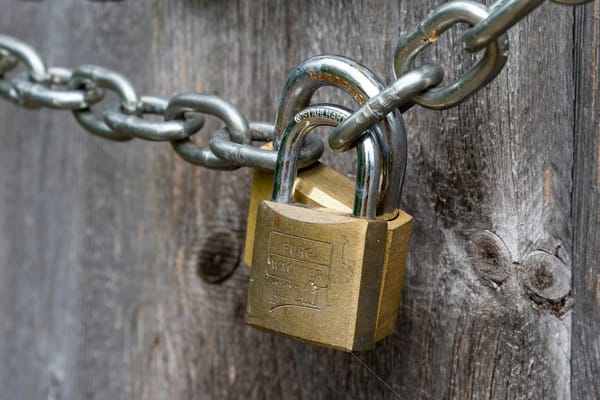A brass padlock on a chain against weathered wood